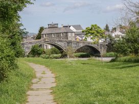 A stone arch bridge over a river with buildings and trees in a green grassy area at Mews Cottage in Llanrwst