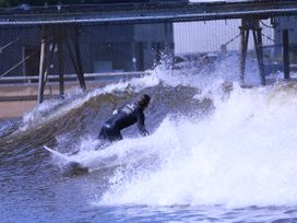 A person surfing on an artificial wave near a metal fence structure at Mews Cottage in Llanrwst