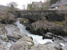 A stone bridge over a river with rocks and houses in the background at Mews Cottage in Llanrwst