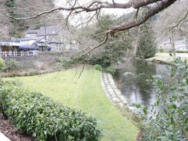 A river flowing beside a grassy bank with stone edging and buildings in the background at Mews Cottage in Llanrwst