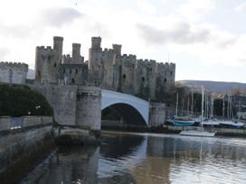 A large stone castle with multiple towers by a river with a stone bridge and boats docked nearby