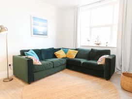 A living room with a green corner sofa yellow and blue cushions a floor lamp a round rug and a window with decorations at Flat 1 Hunstanton