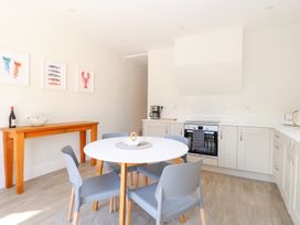A kitchen with white cabinets a round dining table with four gray chairs and a wooden console table with a bottle and bowl on it at Flat 1 in Hunstanton