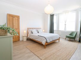 A bedroom with a wooden bed and side tables with lamps a green armchair near windows and a woven rug on the floor at Flat 1 in Hunstanton
