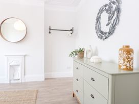 A room with a dresser topped with vases and a plant and a round mirror above a small white fireplace at Flat 1 in Hunstanton