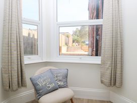 A corner with a chair and two pillows in front of two windows with striped curtains at Flat 1 in Hunstanton