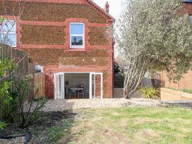 A backyard with a tree and grass leading to a brick house with open folding doors at Flat 1 in Hunstanton