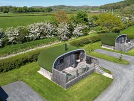 Two cabins with grass roofs and wooden exteriors in a green outdoor area at High Longlands in Cartmel