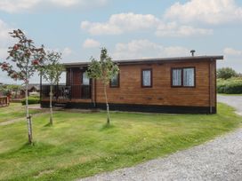 A log cabin with trees and grass at 16 Forest Lodge in Chwilog