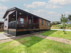 A wooden lodge with a deck and pathway at 16 Forest Lodge in Chwilog