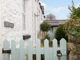 A light blue wooden gate in front of a white textured stone house with a green garden and a door at Ty Croes in St George near Bodelwyddan