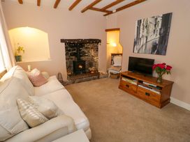 A living room with a white sofa a small wood burning stove and a wooden tv stand with a television and flowers at Ty Croes in St George near Bodelwyddan