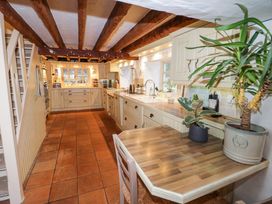 A kitchen with wooden beams, tiled floor, cream cabinets, a wooden countertop, plants on the table and under the stairs at Ty Croes St George near Bodelwyddan
