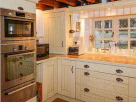 A kitchen corner with built in ovens a microwave toaster wooden cabinets and a window with decorations at Ty Croes in St George near Bodelwyddan