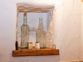 Two decorative glass bottles and two small containers on a wooden shelf inset in a textured wall at Ty Croes St George near Bodelwyddan