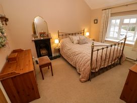 A bedroom with a double metal bed a wooden dresser a stool a fireplace and a window at Ty Croes in St George near Bodelwyddan