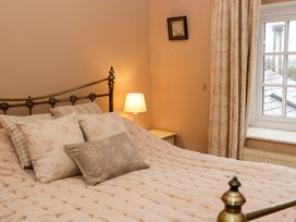 A bedroom with a bed with multiple decorative pillows a bedside table with a lamp floral curtains and a window at Ty Croes in St George near Bodelwyddan
