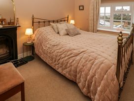 A bedroom with a brass bed frame a padded beige comforter bedside lamps and a window at Ty Croes in St George near Bodelwyddan