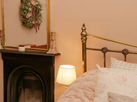 A bedroom corner with a brass bed, floral pillows, a small lamp, and a black fireplace with a mirror and decorative items on the mantel at Ty Croes in St George near Bodelwyddan