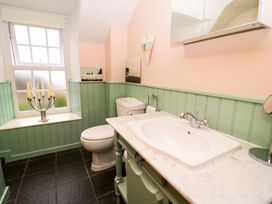 A bathroom with a toilet sink and cabinet a window with a candle holder on the sill and green paneling on the walls at Ty Croes in St George near Bodelwyddan
