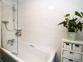 A bathroom with a bathtub shower combination a small shelf with towels and toiletries a white cabinet with wicker drawers and a potted plant at Ty Croes in St George near Bodelwyddan