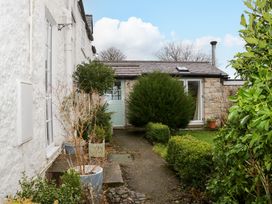 A pathway with potted plants and bushes leading to a small stone building with a green door at Ty Croes in St George near Bodelwyddan
