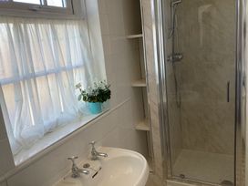 A bathroom with a sink and faucet next to a shower enclosure and window with sheer curtains and a potted plant at Ty Croes in St George near Bodelwyddan