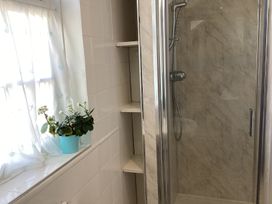 A bathroom with a window with white curtains and a blue flower pot next to a shower with a glass door at Ty Croes in St George near Bodelwyddan