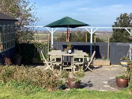 An outdoor patio area with a wooden table and chairs under a green umbrella surrounded by plants and garden containers at Ty Croes in St George near Bodelwyddan