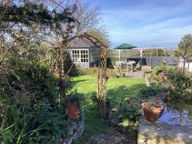 A garden with a wooden archway leading to a lawn a blue garden shed a stone patio with table chairs and an umbrella and a pond with potted plants at Ty Croes in St George near Bodelwyddan