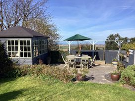 A garden with a small wooden gazebo a patio table with six chairs and a green umbrella at Ty Croes in St George near Bodelwyddan