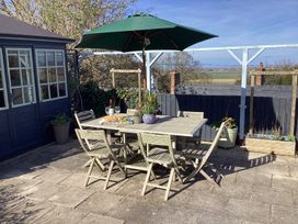 An outdoor patio with a wooden table and six chairs under a green umbrella with a bottle of wine bread grapes and plants nearby at Ty Croes in St George near Bodelwyddan