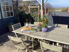 An outdoor wooden table with chairs a bottle of wine two wine glasses a loaf of bread grapes and potted plants at Ty Croes in St George near Bodelwyddan