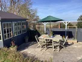 A patio with a wooden table and chairs with a green umbrella and a shed on the side at Ty Croes in St George near Bodelwyddan