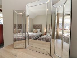 A mirrored dressing table reflecting a bedroom with a bed lamp and window at Beaconsfield Cottage in Burniston near Scalby