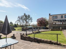 An outdoor patio with a table and closed umbrella beside a small grassy area with stone walls and a house in the background at Beaconsfield Cottage in Burniston near Scalby