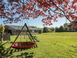 A garden with a red circular swing a wooden slide a picnic table and a small soccer goal under a tree with red leaves at Beaconsfield Cottage in Burniston near Scalby
