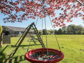 A playground with a red round swing and climbing frame in a grassy field with a barn in the background at Beaconsfield Cottage Burniston near Scalby