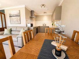 A dining room with a dining table and kitchen in view at 6 Coedrath Park - Swn y Mor in Saundersfoot
