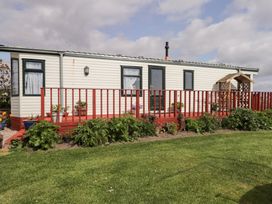 A single-story mobile home with windows door a red wooden deck and green plants in front with grass at The Cabin in Occumster near Lybster