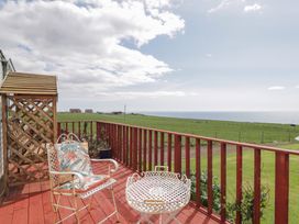 A wooden deck with two chairs and a table overlooking green fields and the sea at The Cabin in Occumster near Lybster