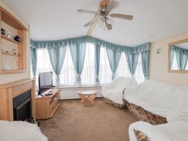A living room with a ceiling fan a television on a wooden stand a glass coffee table and sofas with white covers at The Cabin in Occumster near Lybster