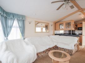 A living room with a sectional sofa covered with white throws a glass coffee table a ceiling fan and blue curtains at The Cabin in Occumster near Lybster