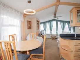 A living room with a round dining table and chairs a small coffee table a television and large windows with blue curtains at The Cabin in Occumster near Lybster