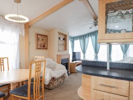 A dining table with four wooden chairs next to a sofa with a white throw in a living room with a fireplace and a television at The Cabin in Occumster near Lybster