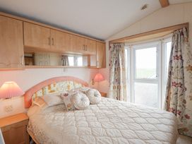 A bedroom with a bed with pillows bedside tables with lamps and a window with floral curtains at The Cabin in Occumster near Lybster