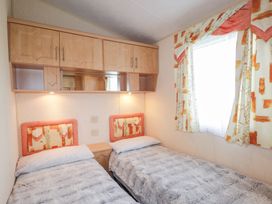 A bedroom with two single beds side by side under wooden cabinets and a window with patterned curtains at The Cabin in Occumster near Lybster