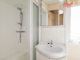 A bathroom with a shower area, a sink with a cabinet, a mirror, and a window at The Cabin in Occumster near Lybster