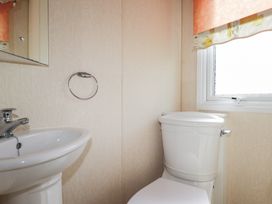 A bathroom with a sink a toilet a small window with a curtain and a towel ring on the wall at The Cabin in Occumster near Lybster