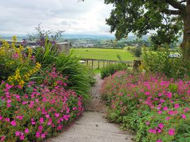 A garden path surrounded by flowers leading to a green field at The Journeyman Luxury Shepherds Hut in Barnoldswick